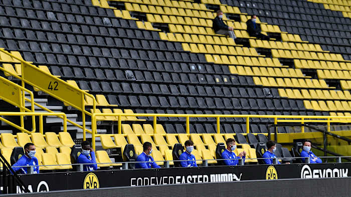 Schalke substitutes sit spread apart in the Dortmund stands